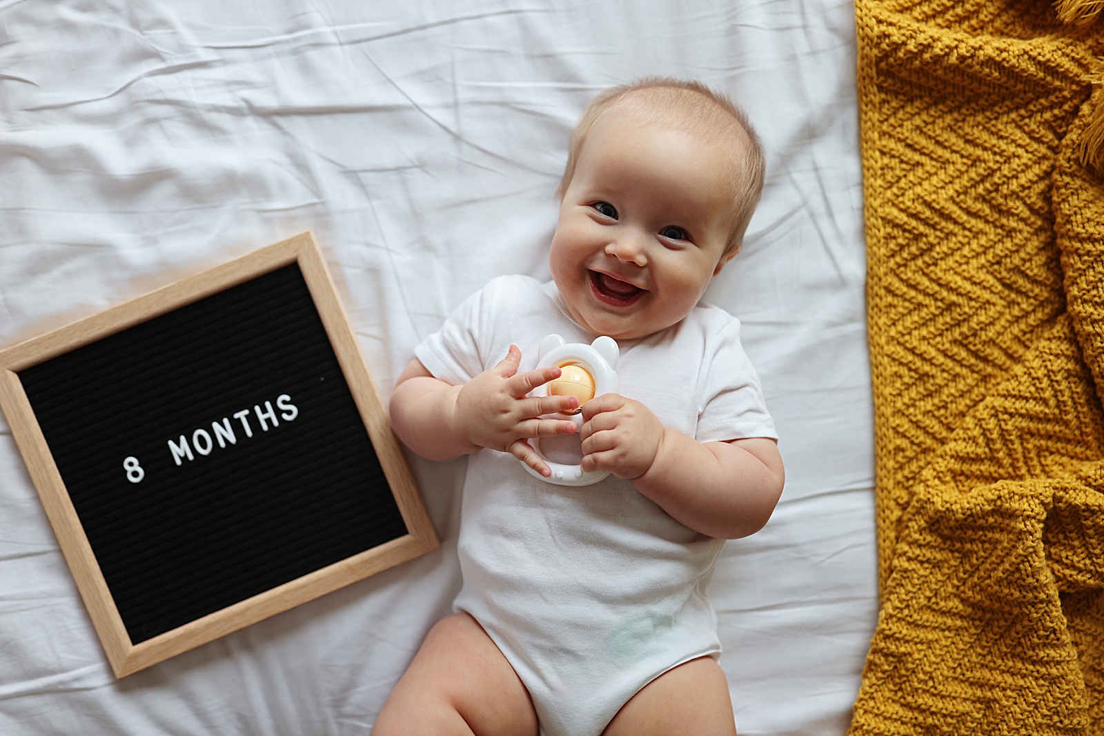 A baby lays beside a letter board for a monthly milestone photo for her baby book.