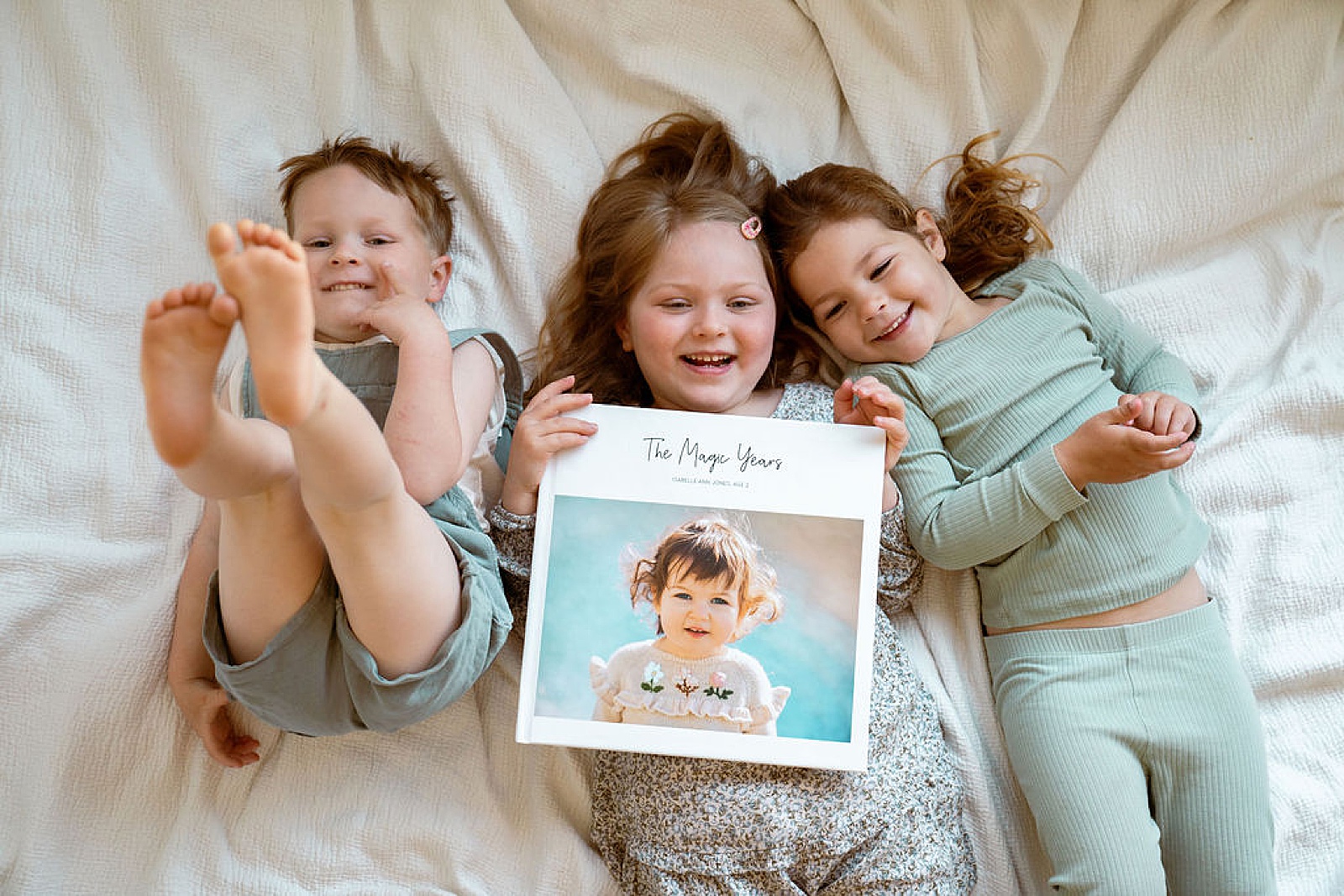 Three toddlers hold up a memory book containing interview questions for preschoolers.