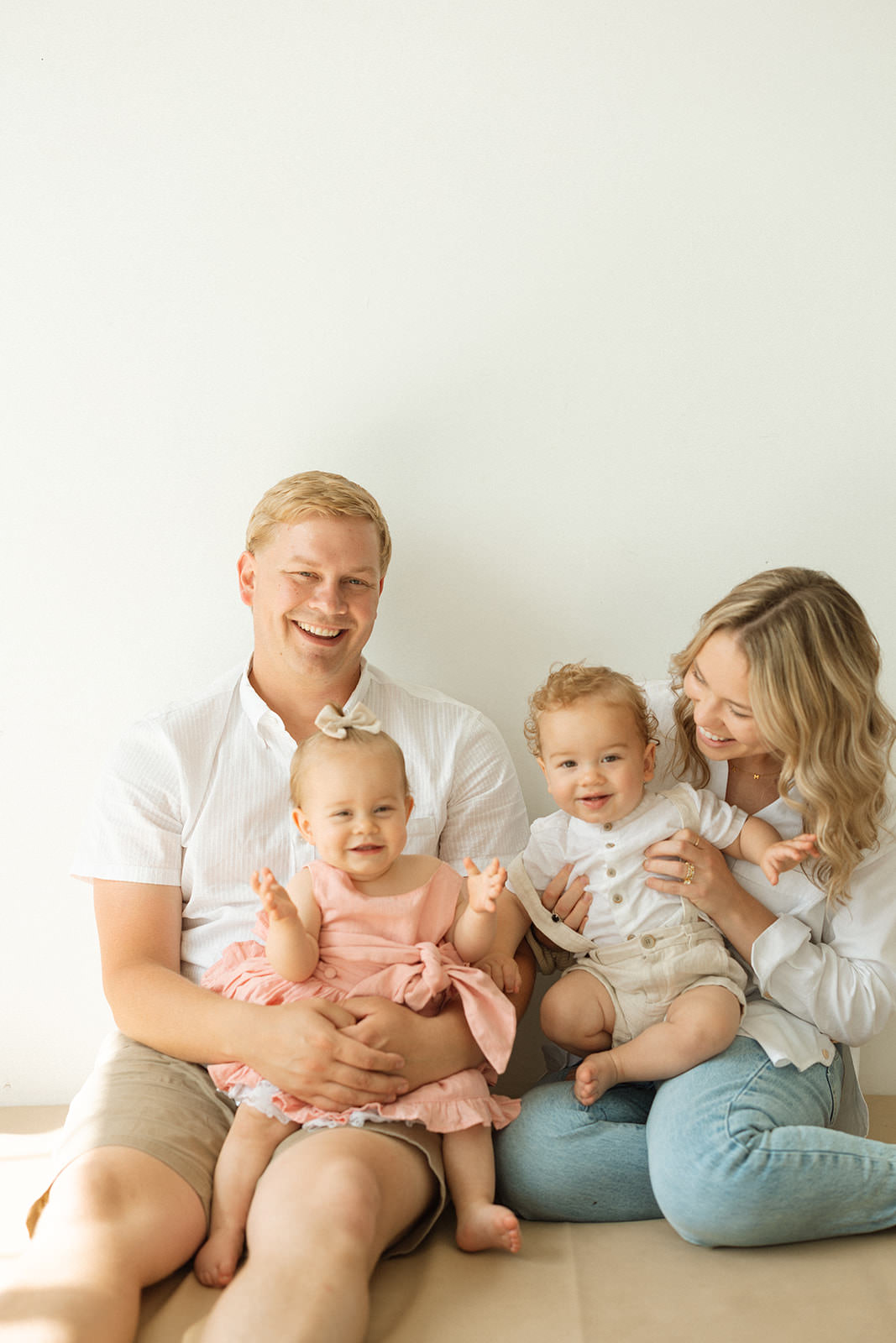 A mother and father hold their twins for a milestone photoshoot in a studio.