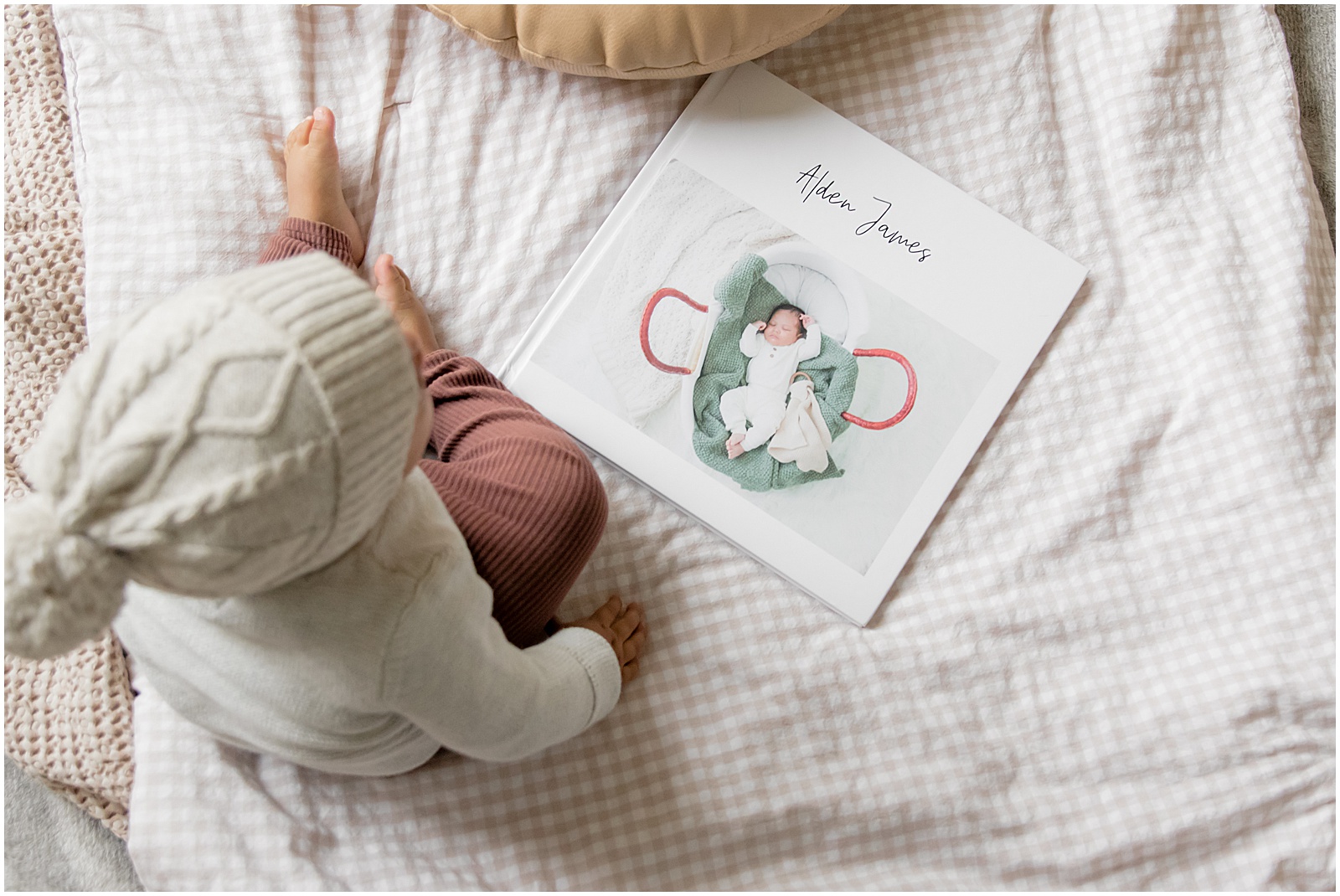 A baby sits on a bed beside a custom baby book.