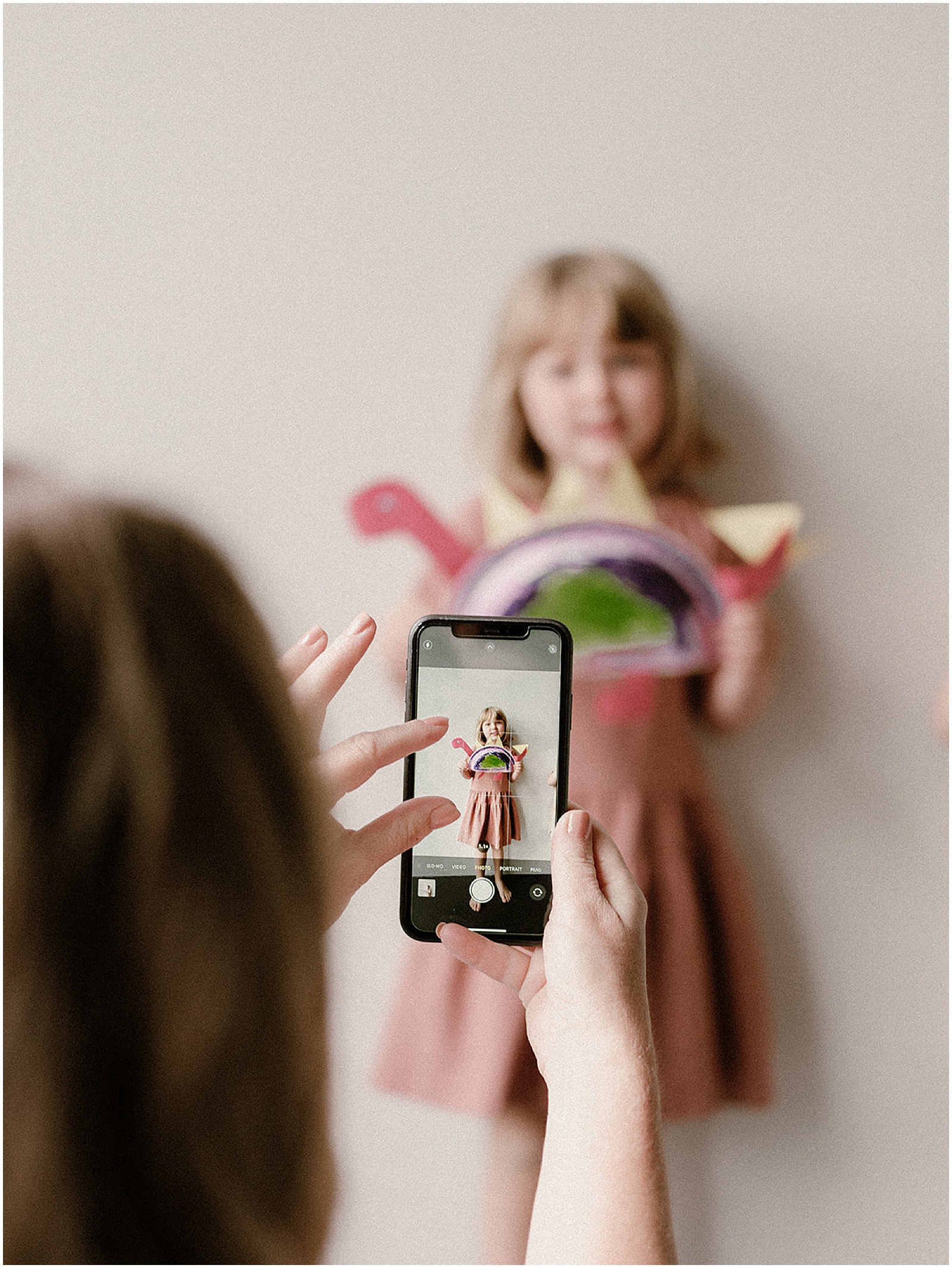 A mother photographs her child holding artwork for a custom memory book.