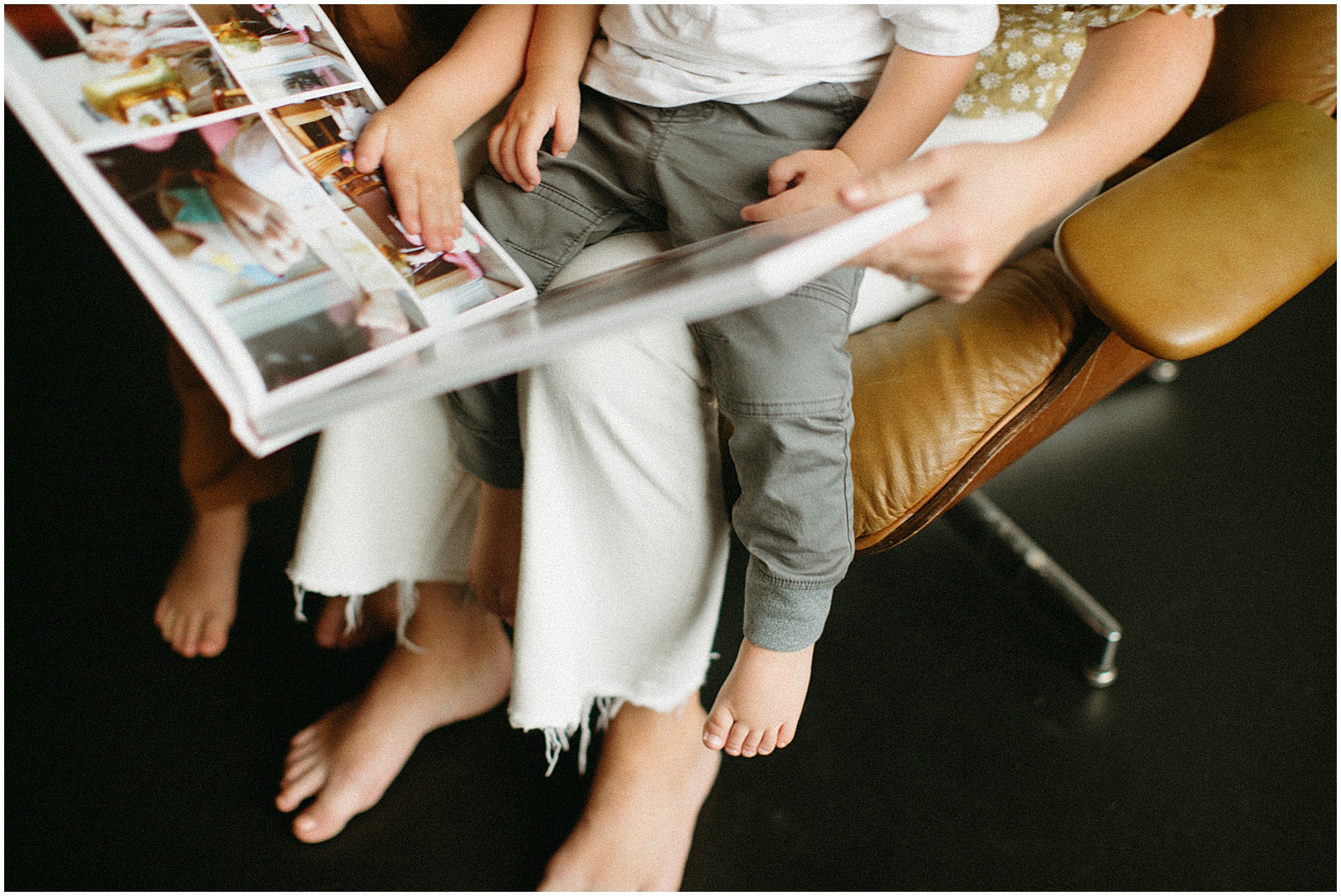 A child sits on his mother's lap looking through a book of photo book ideas.