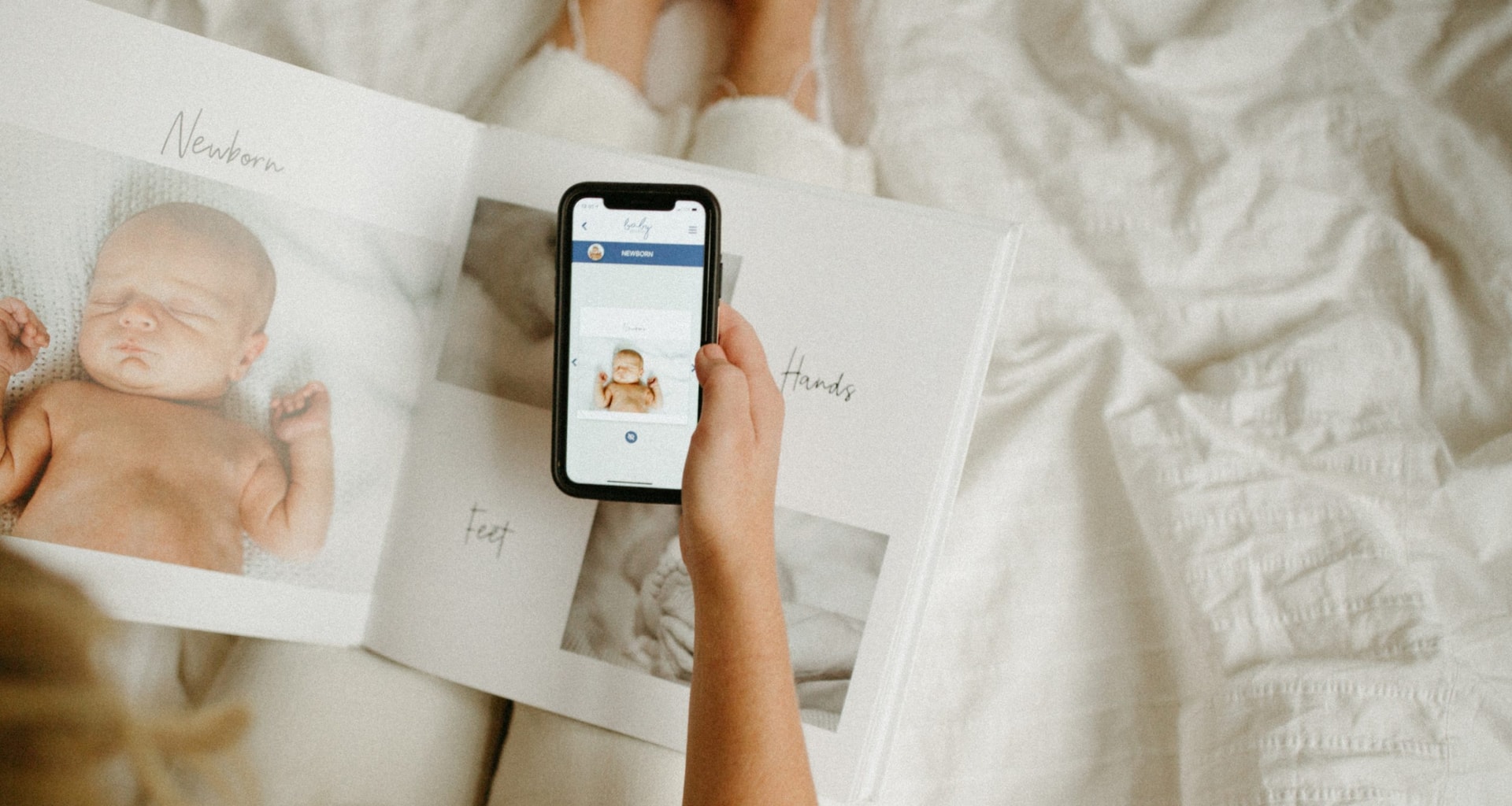 Hand holding a mobile phone showing baby book app screen and modern baby book on lap