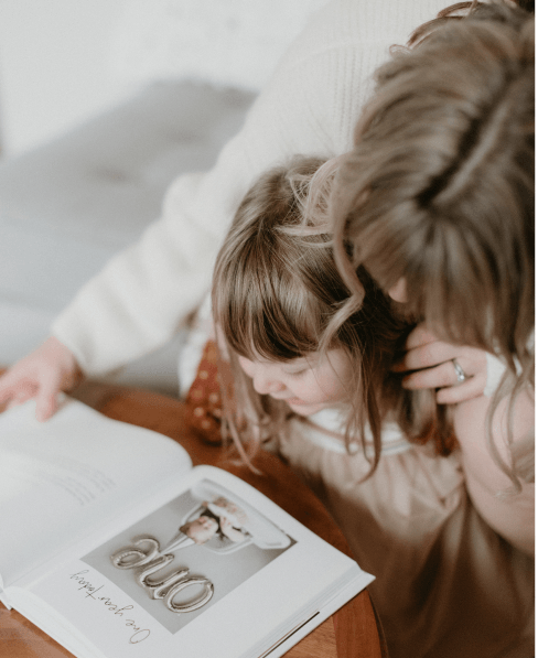 Mom and toddler looking at baby's first birthday page of modern baby book on the table