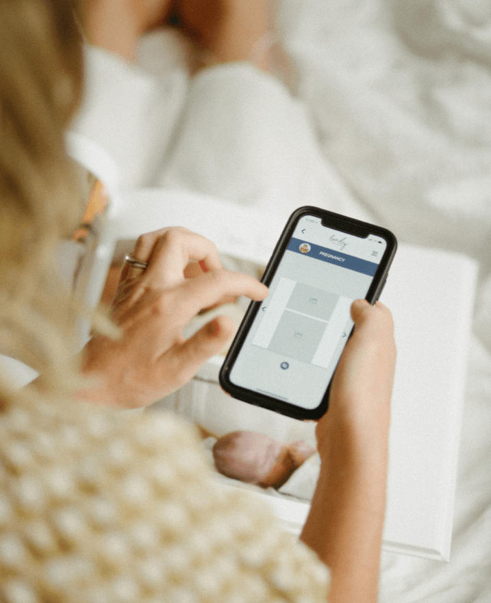 Hands holding phone with baby book app on screen and baby's first year book behind phone